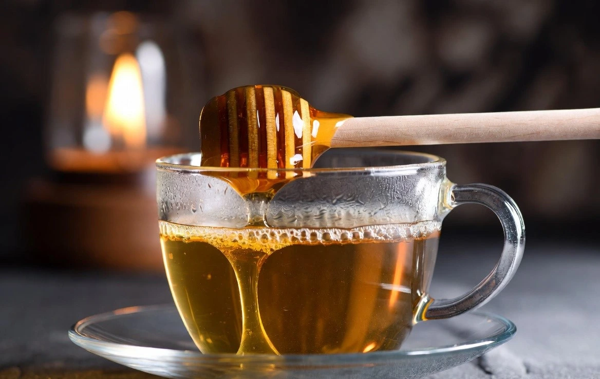 Raw honey dripping into a cup of tea – natural remedy and wellness concept